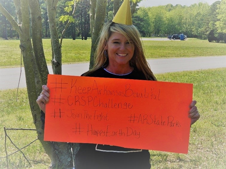 Smiling park employee in party hat holding orange poster with hashtags